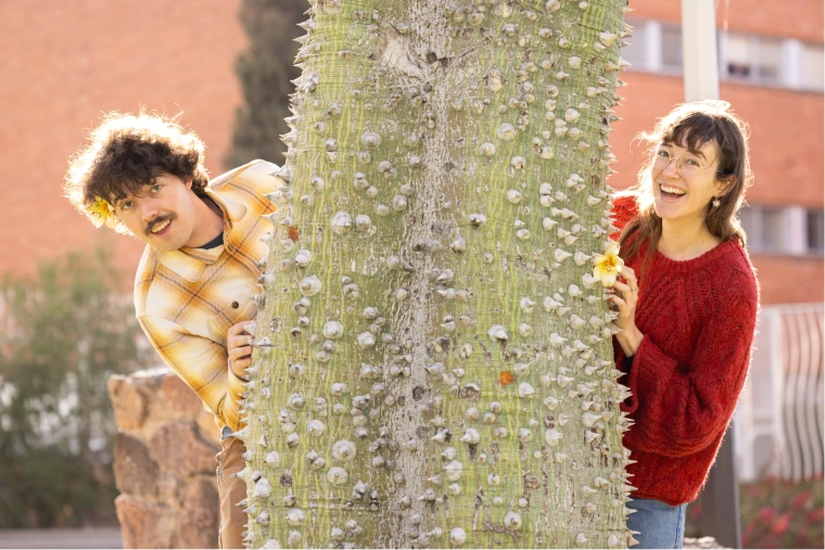 A couple peeking at both sides of a tree 