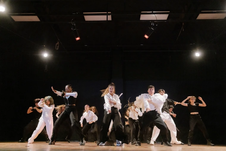 Large dance group in coordinated black and white outfits performs a powerful routine in perfect formation on stage.