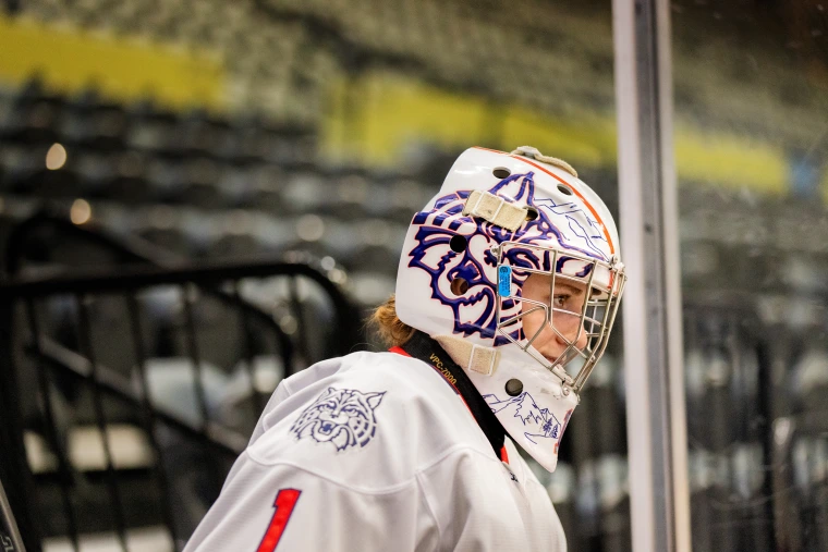 Arizona goalie in a custom-designed Wildcat helmet stands alert near the boards, watching the game.