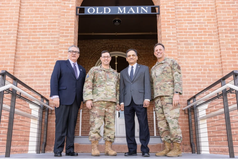 Four individuals pose in front of the University of Arizona’s Old Main building, including two in military uniforms and two in suits.