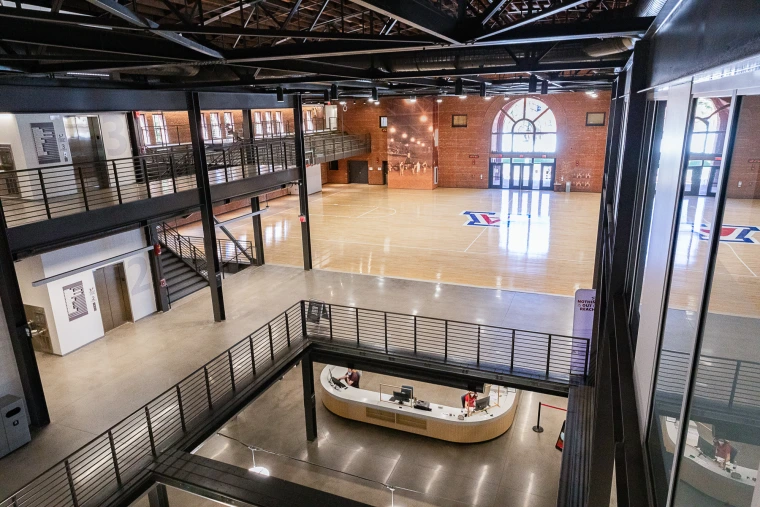 Interior view of Bear Down Gym at the University of Arizona, featuring a central basketball court, open gathering spaces and multiple levels connected by stairways and walkways.
