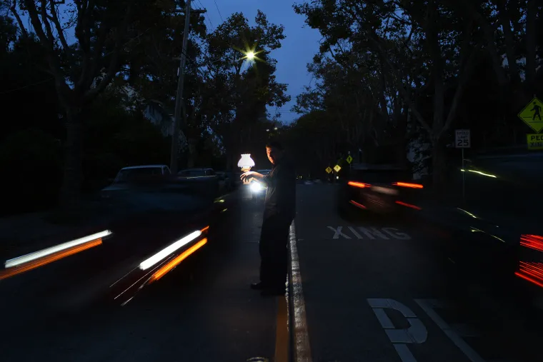 A photograph of Javier Zamora with a lamp, and cars on both sides passing him at night