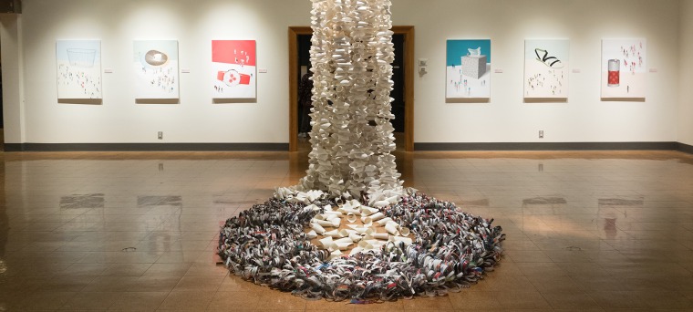 A photograph of the paper sculpture draping onto the floor, surrounded by canvases of Xinyu Zhang's art