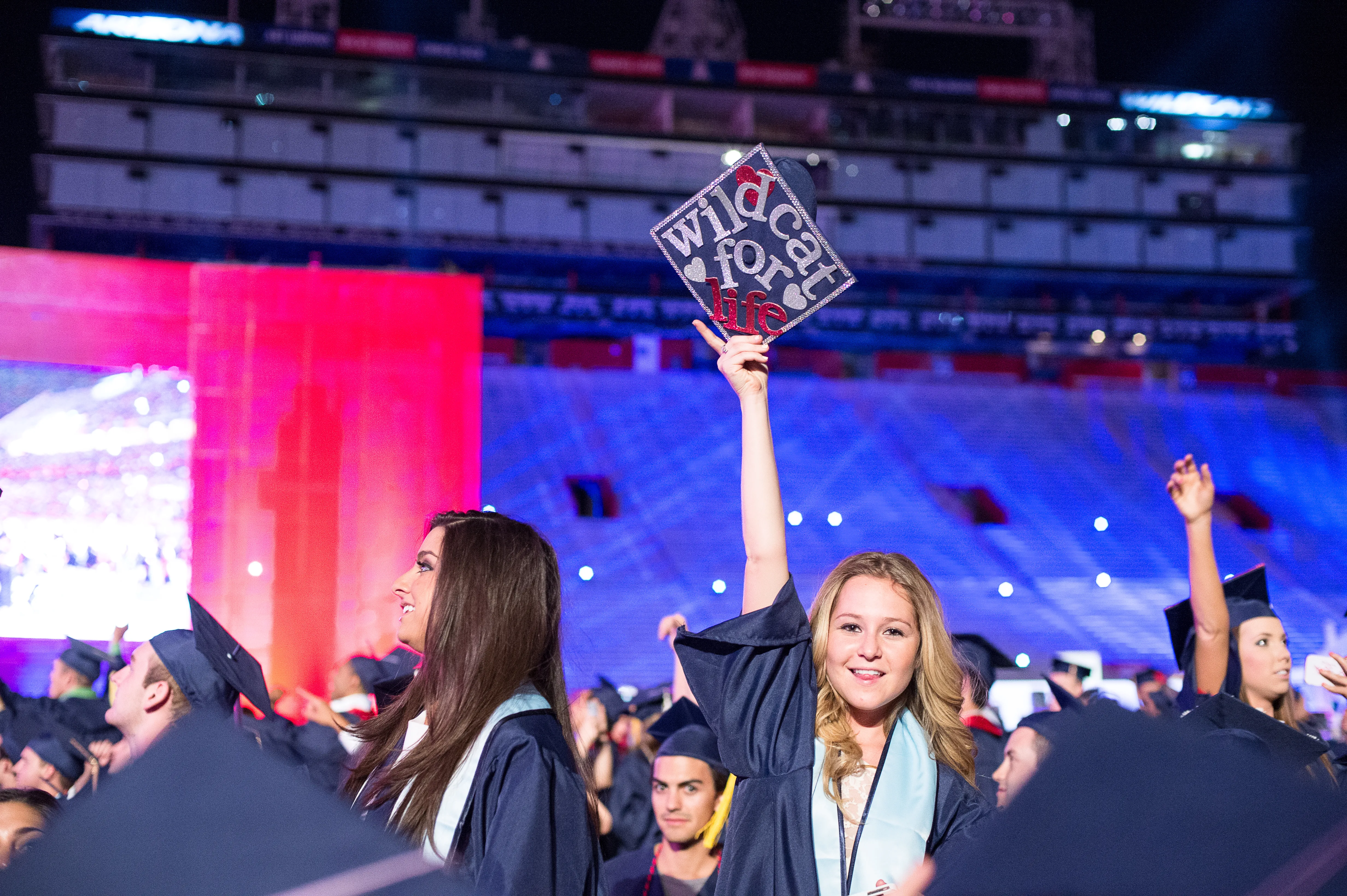 Woman in cap and gown at Commencement ceremony holding a cap that says Wildcat for Life