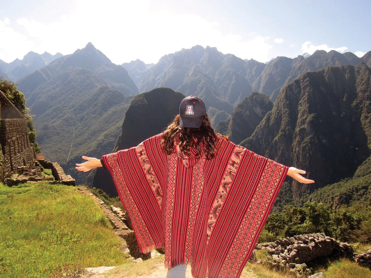 A photograph of Paulina Cabrera standing, wearing a poncho and University of Arizona baseball cap