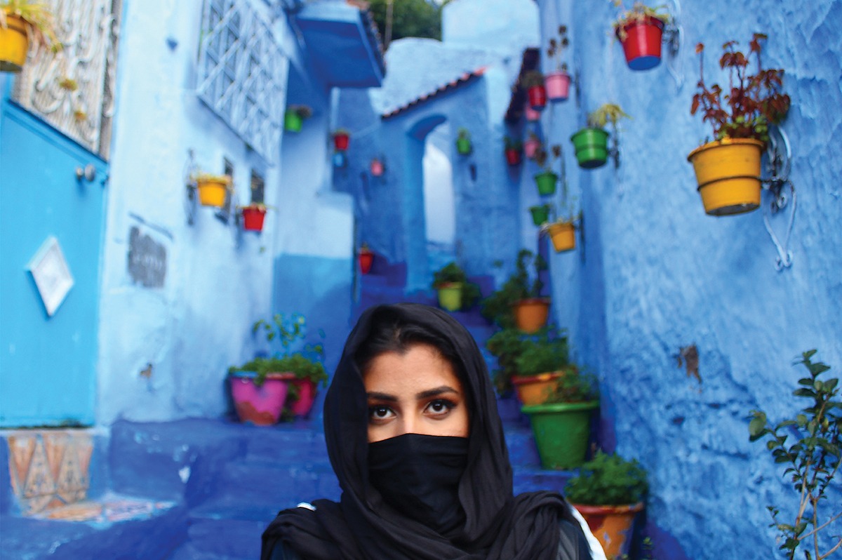 A photograph of Simran Heer walking through a walkway surrounded by blue walls