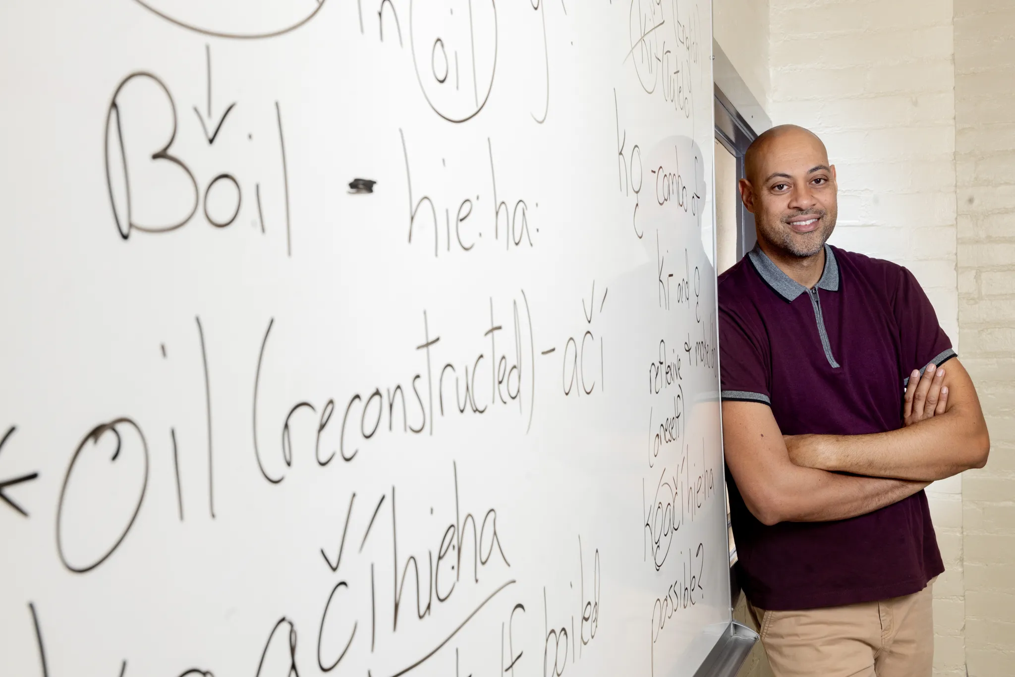 Corey Roberts with his arms crossed smiling next to a white board