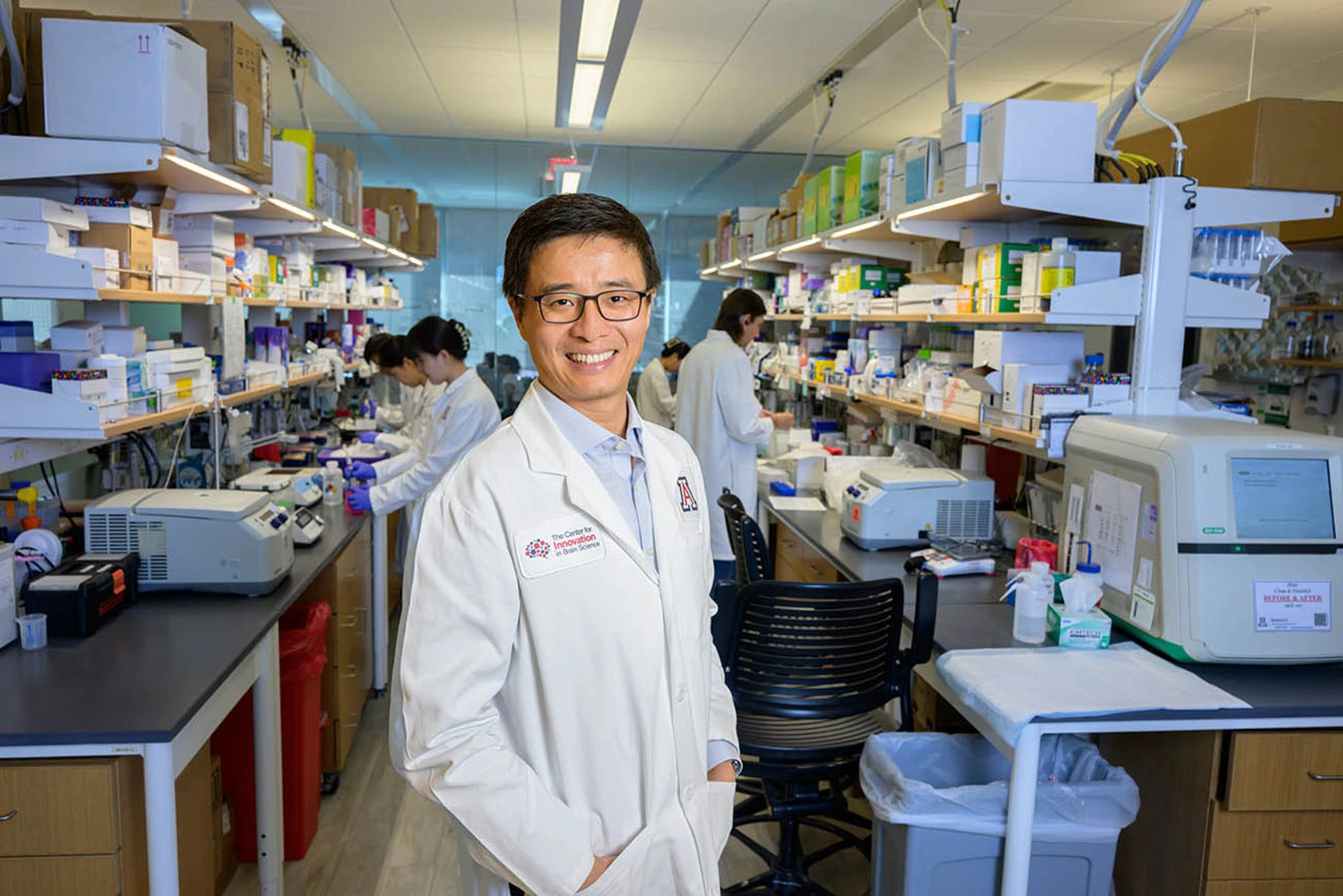 Fei Yin smiling and looking at the camera while standing in his lab 