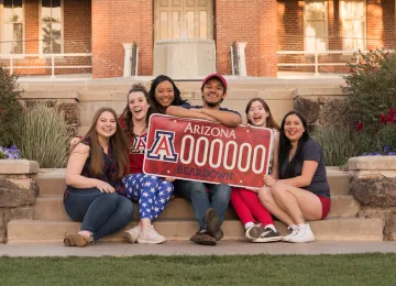 Students sitting in front of Old Main holding an oversized license plate