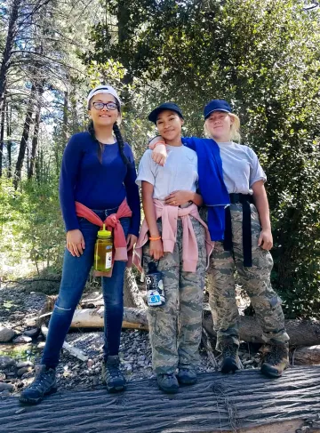 Three girls standing on log in the woods