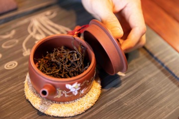 Hand removes lid from gaiwan full of brewing tea