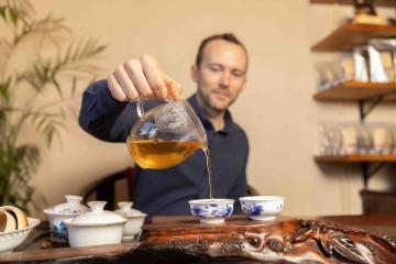 Man pours tea from glass teapot into porcelain teacups