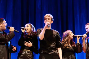 Group of vocalists sings into microphone in acapella performance