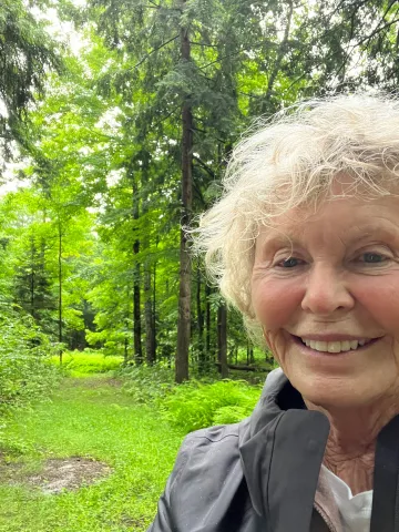 Woman smiles against a green forest backdrop in a selfie style portrait