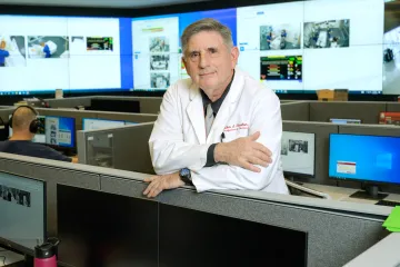 A photograph of a man smiling with his arms crossed over a desk 