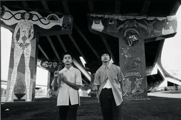 A photograph of two men standing under an underpass surrounded by graffiti 