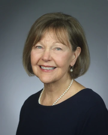 Christine smiling, wearing a black top with pearl earrings and a pearl necklace 