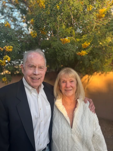 Don, who is wearing a suit, is smiling, with his arm around Susan, who is wearing a white sweater