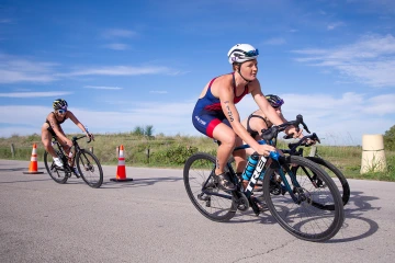 Arizona triathlete leads a pack of cyclists during a race, wearing a helmet and race bib with competitors following closely behind.