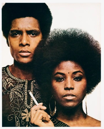 A close-up portrait of two serious-looking people, with the woman holding a cigarette.