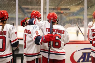 Two Arizona hockey players, with one labeled “THOMPSON,” stand arm-in-arm at the bench watching the rink.