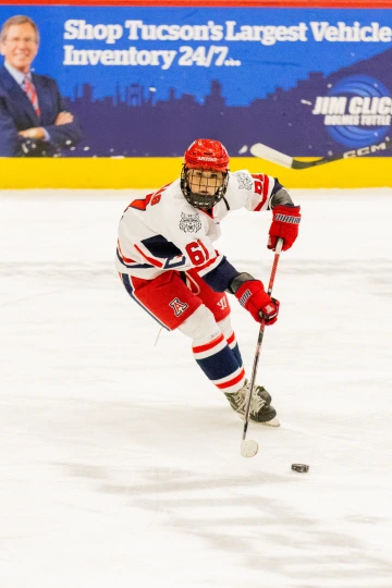 Arizona hockey player skates toward the puck mid-play, with an ad for a local car dealership visible in the background.