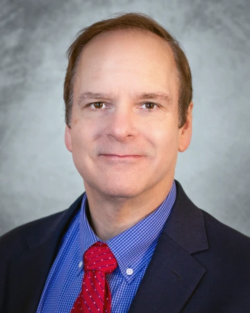A headshot of David Ebert in a suit and tie. The background is gray.