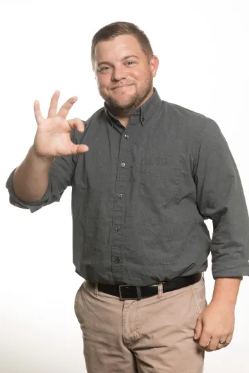 A photograph of Adam Muszynski, smiling and holding up the "Wildcat" sign