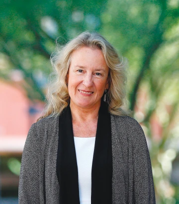 A photograph of Carol Barnes standing in front of a green walkway