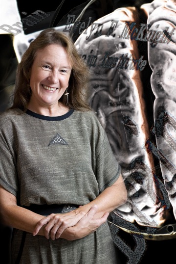 A photograph of Carol Barnes posing in front of a projection of a brain 