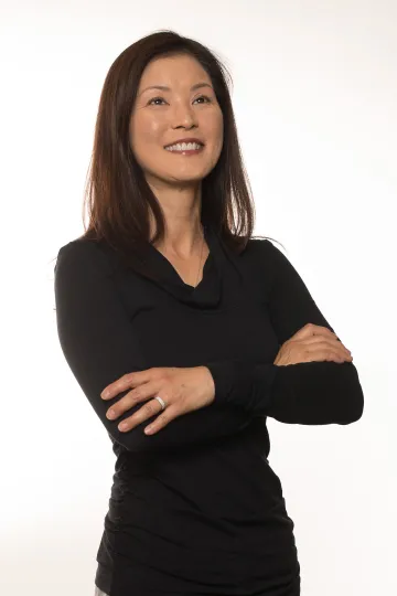 A photograph of Shirley Geile, looking up, smiling, with her arms crossed