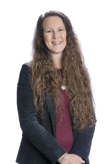 A photograph of Mary Clouser smiling with her arms crossed in the front of her body