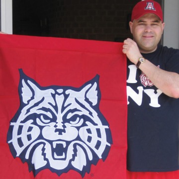 A photograph of Jeffery Plevan holding a Wildcat flag and wearing an "I 'Wildcat' NY" shirt.