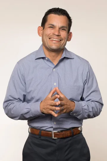 A photograph of Eric Vorrie, smiling with his hands confidently put together