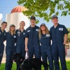 A group of people in coveralls standing in front of siloes on a farm